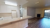 This single-floor residence offers a thoughtfully designed open-concept layout that connects the kitchen and living areas into one cohesive, functional space. The kitchen is equipped with white cabinetry, a full-size refrigerator, and a generous peninsula countertop with a light stone finish that serves as both a prep surface and a casual breakfast bar — effectively bridging the kitchen and living room. A bi-fold door closet is conveniently accessible just off the kitchen area. The living room is anchored by a classic fireplace with a white surround, adding warmth and character to the space. Rich, dark hardwood-style flooring flows throughout the main living areas, providing a striking contrast against the light grey walls and white trim. The textured ceiling adds a traditional touch, while flush-mounted lighting ensures the space is well lit. The neutral color palette throughout creates a clean, inviting atmosphere that is both versatile and easy to personalize. The open floor plan maximizes the sense of space, making this residence feel airy and connected from one end to the other.