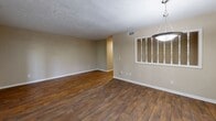 Located at Lansbury Village Drive in Atlanta, GA, this one-bedroom, two-bathroom unit offers a well-organized single-floor layout designed for comfortable everyday living. Rich hardwood-style flooring runs throughout, creating a warm, cohesive look that ties each room together.

The living area is generously proportioned, featuring a textured ceiling, neutral warm-toned walls, and a decorative spindle partition that visually separates it from the dining area. A pendant light fixture anchors the dining space, while French doors along one wall provide natural light and direct access to an outdoor patio.

The kitchen is a standout feature, showcasing dark espresso cabinetry with sleek hardware, marble-look countertops, a mosaic tile backsplash, and black appliances including a range and refrigerator. Track lighting and a window overlooking greenery enhance both functionality and ambiance.

The spacious primary bedroom accommodates large furnishings comfortably, equipped with a ceiling fan with light kit and two closet doors. Natural light enters through multiple windows. Both bathrooms continue the hardwood-style flooring and feature tiled tub-shower surrounds. A connecting hallway links the bathroom spaces efficiently, completing a practical and well-appointed floor plan.
