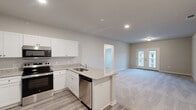 Located at 2308 Holiday Loop in Reidsville, NC, this single-story, one-bedroom, one-bathroom home offers a thoughtfully designed layout ideal for comfortable everyday living. The open-concept main area seamlessly combines the kitchen, dining, and living room into one cohesive space. The kitchen is outfitted with crisp white shaker-style cabinetry, granite-look countertops, a peninsula with a stainless steel sink, and a full suite of stainless steel appliances including a refrigerator, range, microwave, and dishwasher. Luxury vinyl plank flooring runs through the kitchen and entry areas, while plush carpeting extends across the living and bedroom spaces. The living room is bright and open, anchored by French doors that lead to a private patio and allow natural light to fill the room. The generously sized primary bedroom features soaring ceilings, a ceiling fan, and access to two closets, including a walk-in. The bathroom includes a walk-in shower with built-in shelving and a granite-top vanity. A dedicated laundry room with wire shelving and washer/dryer hookups adds everyday convenience. Neutral tones and recessed lighting throughout give the home a clean, modern aesthetic.