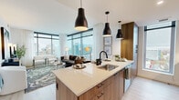 Located at 12004 Inspiration St in Reston, VA, this thoughtfully designed 2-bedroom, 2-bathroom residence offers a refined living experience through a seamless blend of modern architecture and high-quality finishes. The open-concept kitchen and living area serves as the heart of the home, anchored by a large center island with a sleek quartz countertop, warm wood cabinetry, stainless steel appliances, and bold matte black pendant lighting. The living room is a standout, with expansive floor-to-ceiling windows wrapping the corner of the space and delivering sweeping panoramic views of the Reston skyline, bathing the interior in abundant natural light. Light wood flooring flows throughout, enhancing the bright and airy atmosphere. The primary bedroom offers a generous footprint with large windows, views of the surrounding cityscape, and direct access to an en-suite bathroom featuring a wood-toned vanity, white quartz counters, black fixtures, and a walk-in closet with built-in shelving. The second bedroom is equally well-appointed, providing comfort and versatility. A hallway connects the rooms efficiently, completing the functional and elegant layout of this contemporary Reston residence.