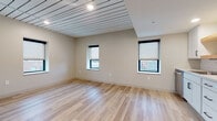 Located at 503 E Cesar E Chavez Ave in Lansing, Michigan, this single-floor unit showcases modern construction with clean, contemporary finishes throughout. Light-toned luxury vinyl plank flooring runs seamlessly across the entire space, complementing the neutral wall tones and creating a bright, cohesive aesthetic.

The open living area is a standout feature, boasting a distinctive slatted ceiling design with recessed lighting and multiple windows fitted with roller shades that allow for ample natural light and views of the surrounding neighborhood. The space is generously proportioned, offering flexible arrangement possibilities.

The kitchen is well-appointed with white shaker-style cabinetry, stainless steel appliances including a range, over-the-range microwave, refrigerator, and dishwasher, and a classic white subway tile backsplash. A stacked washer and dryer unit is conveniently integrated into the kitchen area.

The bedroom features the same slatted ceiling detail as the living area, multiple windows for natural light, and a sliding-door closet with built-in shelving and hanging rods, providing practical storage.

The bathroom is finished with white cabinetry, a quartz-style countertop, an undermount sink, and a full tub-shower combination, all presented in a clean, minimalist style. The overall ambiance of the unit is fresh, modern, and move-in ready.