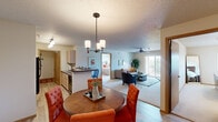 Located at 5008 W Equestrian Pl in Sioux Falls, South Dakota, this 2-bedroom residence offers a thoughtfully designed single-floor layout that balances comfort and functionality. Upon entry, the dining area welcomes you with warm hardwood-style flooring, a stylish round table, and an elegant pendant chandelier overhead. The open-concept design flows seamlessly into the kitchen, which features light wood cabinetry, black appliances, a breakfast bar with seating, and track lighting — ideal for both cooking and casual entertaining. The adjacent living room is generously sized, with plush carpet, a ceiling fan, and sliding glass doors that open to a private balcony, allowing for ample natural light and outdoor views. Both bedrooms are comfortably scaled, each featuring carpeted floors, natural light from windows with neighborhood views, and a textured ceiling. The full bathroom includes a vanity with storage, a tub/shower combination, and hardwood-style flooring. A dedicated in-unit laundry room with full-size washer and dryer adds everyday convenience. Throughout the residence, neutral tones and warm wood accents create a cohesive, inviting ambiance suited to a variety of lifestyles.