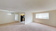 This single-floor residence offers a clean, functional layout designed for comfortable everyday living. The main living area is generously sized, featuring soft wall-to-wall carpeting, neutral cream-toned walls, and a large window fitted with blinds that allows natural light to fill the room. The space flows openly toward a dining area, distinguished by a classic chandelier overhead, creating a natural separation between living and dining zones.

The kitchen is practical and well-appointed, featuring light wood cabinetry with ample upper and lower storage, grey laminate countertops, and a full suite of black appliances including a range, built-in microwave, refrigerator, and dishwasher. A window above the sink provides additional natural light, while tile flooring adds easy-care durability to the space.

The bedroom is a comfortable, carpeted retreat with two doorways leading to a dedicated walk-in closet and an additional storage area, offering excellent organization options. The bathroom is finished in bright, neutral tones with tile flooring, a combined tub and shower unit, toilet, and a vanity with white countertop. A small window provides ventilation and natural light. Throughout the unit, clean white trim and consistent neutral finishes create a cohesive and move-in ready atmosphere.