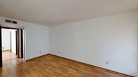 This single-floor unit offers a straightforward and functional layout designed for comfortable everyday living. The main living area greets you upon entry through a six-panel front door, flanked by windows fitted with horizontal blinds that allow natural light to fill the space. Light wood-style flooring runs throughout the main living areas, complemented by white walls and textured ceilings that lend a clean, neutral aesthetic.

Adjacent to the living area, the dining space is distinguished by a modest chandelier overhead and opens directly into the galley-style kitchen. The kitchen features dark wood cabinetry on both sides, light laminate countertops, a double-basin sink, a white electric range, a refrigerator, and a dishwasher, all set on tile flooring. A door at the end of the kitchen provides additional access or storage utility.

The bedroom is a well-proportioned room with the same warm hardwood-style flooring, a window with blinds for natural light, and a ceiling fan with integrated lighting for year-round comfort.

The full bathroom includes a tub-shower combination with tiled surround, a toilet, a single-sink vanity with under-cabinet storage, and a framed mirror, all finished in clean white tones with tile flooring. The overall ambiance of the unit is bright, clean, and move-in ready.