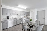 This single-floor residence offers a thoughtfully designed layout that balances functionality and comfort across its principal living spaces. The kitchen is a standout feature, outfitted with grey shaker-style cabinetry, granite-look countertops, and white appliances including a dishwasher, range, and refrigerator. The kitchen flows naturally into a dedicated dining area, where light wood-style flooring continues throughout and a glass-top dining table anchors the space. A secondary kitchenette area with additional cabinetry and sink provides added convenience, with in-unit washer and dryer access nearby.

The living room is bright and welcoming, benefiting from a large sliding glass door that opens to a private balcony with outdoor views, allowing generous natural light to fill the space. Dark hardwood-style flooring grounds the room with a warm contrast to the neutral white walls.

The bedrooms are carpeted for comfort, each receiving natural light through individual windows. One bedroom includes a spacious walk-in closet with wire shelving. Both bathrooms are finished with grey vanity cabinetry, granite-look countertops, and tub-shower combinations with white tile surrounds. An additional carpeted room with a window serves well as a home office or den.