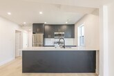 Located at 271 Madison Ave S in Kitchener, Ontario, this thoughtfully designed two-bedroom, one-bathroom unit offers a clean, contemporary aesthetic across a single floor. Light-toned hardwood flooring runs throughout, unifying the space and enhancing its bright, airy feel.

The kitchen is the standout feature of the home, showcasing bold navy cabinetry accented with brushed gold hardware and paired with sleek white quartz countertops. A large peninsula with a double undermount sink and matte black faucet provides additional workspace and casual seating. Stainless steel appliances — including a refrigerator, stove, and built-in microwave — complete the modern culinary setup. A window above the counter allows natural light to fill the space.

The two bedrooms are clean and neutral, finished in soft white tones with light hardwood flooring and windows that bring in natural daylight and neighbourhood views. The rooms offer a calm, versatile canvas suitable for a variety of layouts.

The bathroom is elegantly appointed, featuring a glass-enclosed walk-in shower clad in large-format marble-look tile, complemented by matte black fixtures including a rain showerhead and hardware. A hallway connects the rooms efficiently, keeping the layout practical and well-organized. Overall, the unit presents a polished, modern finish throughout.