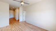 Located at 1803 S 46th Street in Rogers, Arkansas, this thoughtfully designed 2-bedroom, 1-bathroom unit offers a clean, modern aesthetic across a single floor. The interior is finished with light-toned luxury vinyl plank flooring throughout the main living areas, complemented by neutral white walls that create a bright and airy atmosphere. Each room is equipped with a ceiling fan, enhancing comfort and airflow year-round.

The spacious primary bedroom features plush carpeting, a ceiling fan, and a large window with a roller shade that invites ample natural light and outdoor views. The second bedroom mirrors the same clean design with carpeted floors, natural light, and its own ceiling fan. Both rooms offer a calm, neutral palette ideal for personalizing.

The bathroom is finished with wood-look flooring, a walk-in tiled shower with subway tile surround and brushed nickel fixtures, a vanity with a white countertop, and contemporary hardware throughout. A dedicated laundry room houses a stacked Electrolux washer and dryer set alongside built-in wire shelving, maximizing storage and convenience. The kitchen, visible in the dollhouse view, features white cabinetry and stainless steel appliances, rounding out this functional and modern living space.