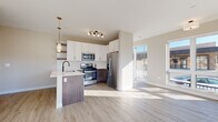 Located at 109 S Main St in Lombard, IL, this single-floor unit offers a thoughtfully designed layout with modern finishes and abundant natural light throughout. The open-concept kitchen and living area serves as the heart of the space, featuring white upper cabinetry paired with dark wood lower cabinets, a white quartz peninsula with an undermount sink, and a full suite of stainless steel appliances including a gas range, built-in microwave, dishwasher, and French door refrigerator. A tile backsplash, open floating shelves, and pendant lighting add refined detail to the kitchen. Light wood-look flooring extends through the main living areas, complementing the neutral warm-toned walls. Oversized windows and a sliding glass door flood the living area with natural light while offering views of the surrounding streetscape. The bedrooms are carpeted and well-lit, with large windows providing additional outdoor views and access to an exterior balcony. A hallway connects the private areas of the unit, which include a full bathroom featuring a glass-enclosed walk-in shower, white vanity with dark countertop, and black hardware accents, as well as a separate water closet. The overall aesthetic is clean, contemporary, and move-in ready.