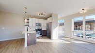 Located at 109 S Main St in Lombard, IL, this single-floor unit offers a thoughtfully designed layout with modern finishes and abundant natural light throughout. The open-concept kitchen and living area serves as the heart of the space, featuring white upper cabinetry paired with dark wood lower cabinets, a white quartz peninsula with an undermount sink, and a full suite of stainless steel appliances including a gas range, built-in microwave, dishwasher, and French door refrigerator. A tile backsplash, open floating shelves, and pendant lighting add refined detail to the kitchen. Light wood-look flooring extends through the main living areas, complementing the neutral warm-toned walls. Oversized windows and a sliding glass door flood the living area with natural light while offering views of the surrounding streetscape. The bedrooms are carpeted and well-lit, with large windows providing additional outdoor views and access to an exterior balcony. A hallway connects the private areas of the unit, which include a full bathroom featuring a glass-enclosed walk-in shower, white vanity with dark countertop, and black hardware accents, as well as a separate water closet. The overall aesthetic is clean, contemporary, and move-in ready.