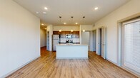 This well-appointed single-floor residence offers a thoughtfully designed open-concept layout that seamlessly connects the living and kitchen areas. The kitchen serves as the centerpiece of the space, anchored by a large island topped with granite countertops and an undermount sink, illuminated by stylish pendant lighting above. Rich dark cabinetry lines the walls, complemented by a classic subway tile backsplash and a full suite of stainless steel appliances, including a refrigerator, range, and microwave. Warm hardwood-style flooring flows throughout the main living areas and hallways, creating a cohesive and inviting atmosphere. Recessed lighting throughout ensures the space is well-lit, while white plantation shutters allow for natural light control in the living area. A built-in shelving nook adds practical storage near the entryway corridor. The bedroom features plush carpeting and a ceiling fan, offering a comfortable retreat. The bathroom is finished with granite countertops, dark cabinetry, and a tiled shower-tub combination with chrome fixtures. A dedicated laundry area with shelving above provides added convenience. Overall, the space presents a clean, modern aesthetic with quality finishes throughout.
