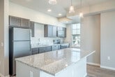 Located at 1055 Simon Crestway in Waunakee, Wisconsin, this well-appointed 2-bedroom, 2-bathroom residence offers a thoughtfully designed single-floor layout with a clean, modern aesthetic throughout. Light-toned hardwood-style flooring flows through the main living areas, complemented by neutral gray walls and crisp white trim that lend a bright, cohesive feel.

The open-concept kitchen serves as the heart of the home, anchored by a large granite-topped island with pendant lighting overhead. Dark espresso cabinetry lines the walls alongside stainless steel appliances, including a refrigerator, range, microwave, and dishwasher, offering both style and function. The kitchen opens naturally toward the living area, which benefits from recessed lighting and a chandelier accent, and extends to a private balcony with outdoor views.

A light-filled hallway connects the bedrooms, each featuring plush carpeting and generous windows that invite natural light. The spacious primary bedroom offers comfortable dimensions and direct access to a private bathroom equipped with a walk-in shower, granite vanity, and dark cabinetry. The second bathroom includes a full tub-shower combination, matching granite countertops, and built-in shelving. Two closets provide ample storage throughout the residence.