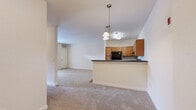 This single-story unit offers a thoughtfully designed layout that maximizes functionality across its comfortable footprint. The open-concept living and kitchen area serves as the heart of the unit, where a peninsula with a dark countertop visually separates the two spaces while maintaining an open, connected feel. The kitchen is equipped with warm honey-toned cabinetry, ample upper and lower storage, dark countertops, and black appliances including a refrigerator and electric range. A pendant chandelier above the peninsula adds a decorative focal point. The living area features neutral carpet, cream-toned walls, and French doors with a transom window above, allowing natural light to filter in and providing access to an outdoor balcony area.

The bedroom is a well-proportioned, carpeted room featuring a ceiling fan, a dedicated closet, and a window with outdoor views, contributing to a bright and airy atmosphere. The bathroom connects conveniently to the hallway and features wood-look tile flooring. A dedicated in-unit laundry area accommodates a full-sized washer and dryer with overhead wire shelving for added storage. Neutral tones and plush carpet throughout lend the unit a cohesive, understated aesthetic.