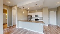 Located at 5050 Transit Rd in Depew, NY, this well-appointed 2-bedroom, 2-bathroom unit offers a thoughtfully designed single-level layout with modern finishes throughout. The open-concept kitchen and living area serves as the heart of the home, anchored by a large peninsula with granite countertops and a built-in sink. Crisp white cabinetry, stainless steel appliances — including a gas range, microwave, and refrigerator — and a trio of elegant pendant lights complete the kitchen's contemporary aesthetic. Light hardwood-style flooring runs throughout the main living areas, adding warmth and cohesion to the space. The primary bedroom features direct access to a private balcony with outdoor views, while the second bedroom benefits from dual windows that flood the room with natural light and offer scenic views of the surrounding landscape. Both bedrooms are finished with plush carpeting for added comfort. The primary bathroom includes a granite-topped vanity, a bathtub/shower combination, and a spacious walk-in closet equipped with wire shelving systems. The second bathroom is equally well-finished with coordinating fixtures and light wood-tone flooring. A neutral color palette and clean architectural lines give the entire unit a bright, modern ambiance.