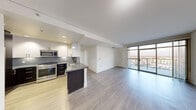 This contemporary single-floor residence showcases a thoughtfully designed open-concept layout with a clean, modern aesthetic. The kitchen is a standout feature, equipped with stainless steel appliances including a gas range, built-in microwave, and full-size refrigerator. Dark espresso cabinetry contrasts elegantly with white upper cabinets and a gray tile backsplash, while the central island provides additional prep space and a double stainless steel sink. Light wood-style flooring flows throughout the main living areas, enhancing the bright, airy atmosphere created by expansive floor-to-ceiling windows. These windows flood the living room with natural light and open to a balcony offering elevated city views. A carpeted bedroom features its own set of floor-to-ceiling windows, a structural column accent, and louvered closet doors. An additional carpeted room provides flexible living space. The primary bathroom includes a soaking tub, a vanity with a gray countertop, white cabinetry, large-format gray tile flooring, and a glass-enclosed shower. A secondary bathroom features a warm wood vanity, white countertop, a globe chandelier, and a glass-enclosed shower. Throughout, the space maintains a cohesive palette of whites and neutral tones, lending a refined and contemporary feel.