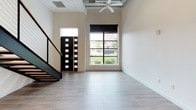 This two-story, 1-bedroom, 1-bathroom residence combines modern design with functional living. The main level greets you with soaring ceilings, light wood-style flooring, and a striking black steel staircase with cable railing. A large multi-pane window floods the living area with natural light and frames outdoor views, while an exposed ceiling with a ceiling fan adds an industrial-chic touch. The sleek, contemporary kitchen features dark lower cabinetry contrasted by crisp white upper cabinets, marble-style countertops, a stainless steel sink, and white appliances including an electric range and over-the-range microwave. The clean, bright bathroom is outfitted with tile flooring, a dark wood vanity with marble-style countertop, and a full tub-shower combination enclosed by a curved glass door. A bold, paneled dark entry door with glass accents makes a strong architectural statement at the entrance. Throughout the residence, a consistent palette of white walls, dark cabinetry, and light flooring creates a cohesive, modern aesthetic that is both stylish and move-in ready.