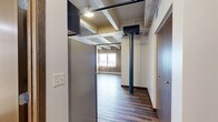 Located on First Ave N in Moorhead, MN, this one-bedroom, one-bathroom unit offers a compelling blend of historic industrial character and modern finishes. The open living area makes a striking impression with exposed wooden ceiling beams, original brick masonry walls, and durable hardwood-style plank flooring that runs throughout the main living space — creating a warm, loft-inspired ambiance.

The kitchen is a standout feature, outfitted with rich dark-stained cabinetry, light-toned countertops, and a full suite of stainless steel appliances including a refrigerator, range, and microwave. The exposed beam ceiling continues into this space, reinforcing the industrial aesthetic while recessed lighting provides practical illumination.

The bedroom features plush carpeting and a full-width closet with dark wood bi-fold doors, offering generous storage. The bathroom includes a clean, all-white walk-in shower unit with chrome fixtures, maintaining a crisp and functional design.

Two hallways connect the rooms efficiently, contributing to a logical and well-organized layout. Throughout the unit, the interplay of raw, reclaimed materials — weathered beams, brick, and aged wood accents — alongside contemporary finishes creates a distinctive and character-rich living environment ideal for those who appreciate industrial-style design.
