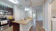 This single-floor, two-bedroom, two-bathroom residence in Ocoee, Florida offers a well-designed open layout with modern finishes throughout. The kitchen serves as a central feature, showcasing rich dark cabinetry, granite countertops, and a full suite of stainless steel appliances including a refrigerator, range, and built-in microwave. A peninsula with pendant lighting above provides additional prep space and creates a natural connection to the living area, which is finished with wood-style flooring that extends through the main living spaces.

Both bedrooms are carpeted and feature ceiling fans. One bedroom offers a sliding glass door opening to a private balcony with outdoor views, while the other provides access to an exterior door with natural light. The two bathrooms are distinctly appointed: one includes a soaking tub and shower combination with tile accents and dark wood vanity, while the second features a walk-in glass-enclosed shower with matching tile detailing and wood-look flooring. A dedicated laundry area accommodates a full-size washer and dryer. Neutral gray tones throughout create a cohesive, contemporary ambiance.