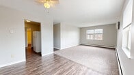 This 2-bedroom, 1-bathroom single-floor unit offers a functional and practical layout that makes efficient use of its available square footage. The open living area greets you upon entry, featuring dark hardwood-style flooring and a ceiling fan overhead. A textured ceiling adds character, while a window allows natural light to filter in with views of the surrounding neighborhood. The flooring transitions to plush carpet in the living zone, creating a comfortable, defined space.

The kitchen is positioned adjacent to the living area and features warm wood cabinetry, providing ample storage. A white refrigerator and stove are included, making the space move-in ready.

A hallway connects the living area to the private quarters, with the spacious primary bedroom offering generous room for furnishings, two sliding-door closets for ample storage, carpeted flooring, and a baseboard heating unit. The second bedroom is similarly well-sized with carpet and a window for natural light. A dedicated area with hardwood-style flooring and electrical outlets suggests a convenient laundry or utility space.

The full bathroom includes a wood-vanity, a tiled shower-tub combo, and hardwood-style flooring. Baseboard heating is found throughout, and a wall-mounted AC unit ensures year-round comfort.