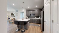 Located in Pensacola, FL, this well-appointed single-floor home offers a thoughtfully designed layout that maximizes both comfort and functionality. The kitchen serves as a standout centerpiece, featuring dark charcoal shaker-style cabinetry, a bold subway tile backsplash, quartz countertops, stainless steel appliances, and a central island with bar seating — ideal for casual dining and entertaining. Light wood-tone flooring runs throughout, tying the spaces together with a warm, cohesive aesthetic. The spacious primary bedroom is bathed in natural light from large windows and includes a ceiling fan, plush area rug, and direct access to two closets, one of which offers generous walk-in storage with wire shelving. The full bathroom is clean and modern, featuring dark cabinetry with a white quartz vanity top, a large mirror, and a full soaking tub. A dedicated office provides a quiet, versatile space with its own window and ceiling fan — well-suited for remote work or study. Crisp white walls and neutral tones throughout contribute to a bright, airy ambiance, while recessed lighting and pendant fixtures add a polished finishing touch to this move-in-ready Pensacola home.