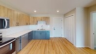 This compact yet well-designed 550 square foot apartment maximizes space efficiency while offering modern amenities. The single-floor layout comprises one bedroom, one bathroom, a combined kitchen and living area, and a dedicated laundry space. The 100 square foot primary bedroom provides a cozy retreat, while the open-concept living area creates a sense of spaciousness.

The kitchen stands out with its contemporary design, featuring a mix of light wood and blue cabinetry, stainless steel appliances, and a sleek white tile backsplash. The L-shaped layout optimizes functionality, offering ample counter space and storage. Adjacent to the kitchen, the living area boasts warm wood flooring that extends throughout the apartment, enhancing visual continuity and warmth.

The bathroom showcases a clean, modern aesthetic with a floating vanity, round mirror, and neutral color palette. In-unit laundry facilities, complete with a washer and dryer, add convenience to daily living. Large windows, including a sliding glass door leading to a balcony, flood the space with natural light and provide outdoor views, expanding the sense of space.

Neutral wall colors and recessed lighting contribute to the apartment's bright, airy ambiance. The thoughtful design and efficient use of space make this apartment an ideal urban dwelling for those seeking a compact yet comfortable living environment.