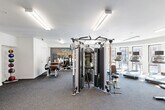 Located at 305 E Front St in Missoula, Montana, this modern fitness center offers a comprehensive workout facility across a single, efficiently organized floor. The space is thoughtfully designed to accommodate a wide range of exercise needs, from cardiovascular training to strength and functional fitness.

The cardio zone is highlighted by a curved, window-lined section that floods the area with natural light and provides open views of the surrounding Missoula cityscape. A row of treadmills and an elliptical trainer are positioned to take full advantage of this bright, airy corner. Overhead, recessed and flush-panel lighting ensures consistent illumination throughout.

The strength training area is well-appointed, featuring a multi-station cable machine, a squat rack, adjustable benches, and a full dumbbell rack spanning a wide range of weights. Kettlebells and medicine balls add versatility to the workout options available. A vibrant orange accent wall adorned with fitness-themed typography serves as a bold, motivational focal point.

A secondary functional training area includes stability balls, foam rollers, and additional cable attachments, supported by a built-in water fountain and hand sanitizer station for user convenience. Dark, durable carpet flooring extends throughout the space, providing both comfort and sound absorption. The overall design is clean and modern, with white walls and bright lighting creating an energetic yet focused workout environment.