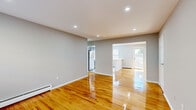 This single-floor residence offers a clean, modern aesthetic defined by gleaming hardwood floors and neutral gray walls throughout. The open living and dining area is generously proportioned, bathed in natural light that reflects off the polished floors, and benefits from recessed lighting overhead. Baseboard heating runs along the walls, ensuring comfort year-round, while a door leads to an outdoor area, adding a sense of openness to the living space.

The kitchen is thoughtfully designed with dark espresso cabinetry, a white countertop peninsula that serves as a natural divider between the kitchen and living area, and a full suite of stainless steel appliances including a gas range, over-the-range microwave, dishwasher, and refrigerator. Light-toned vinyl plank flooring and a window with blinds complete the kitchen's bright, functional character.

The bedrooms are well-sized, each featuring the same warm hardwood flooring and soft gray walls. One bedroom includes a spacious walk-in closet, while another features a window unit air conditioner alongside a baseboard heater for year-round climate control. The classic six-panel white interior doors add a timeless touch throughout the unit. Overall, the space presents a fresh, move-in-ready environment that balances practicality with comfortable, modern living.