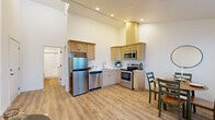 This efficiently designed one-bedroom, one-bathroom unit offers a thoughtfully organized single-floor layout that maximizes every square foot. The open-concept living and dining area is bright and airy, featuring light wood-look flooring, recessed lighting, and crisp white walls that create a clean, modern aesthetic. Large windows and a glass-paned door flood the space with natural light while framing striking waterfront views, with direct access to a private balcony.

The kitchen is well-appointed with light wood cabinetry, stainless steel appliances including a refrigerator, dishwasher, microwave, and electric range, and a double sink. The elevated ceiling above the kitchen adds a sense of openness to this functional cooking space.

The bedroom offers a comfortable, carpeted retreat with soaring angled ceilings, a sliding-door closet, and dual windows that let in natural light. Its quiet, neutral palette promotes a restful atmosphere.

The bathroom is clean and practical, finished with wood-look flooring, a light wood vanity with a white countertop, and a full tub-shower combination. A stacked washer and dryer unit is conveniently located within the bathroom, adding in-unit laundry functionality. Overall, the unit presents a cohesive, modern design with practical amenities and notable waterfront views.