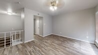 This two-story home in Dallas, TX offers a well-organized layout spread across two floors. The main level features a combined living and dining area with rustic wood-look flooring, neutral gray walls, and ceiling fans that run throughout the home. A white staircase with metal railings connects the floors and serves as a visual focal point from the living area. Vertical blinds along the main floor's sliding door allow for natural light while maintaining privacy. The kitchen is efficiently designed with white cabinetry, granite-look countertops, a coil electric range, and a full-size refrigerator, maximizing the available space. A convenient half bath on the main level includes a granite-topped vanity with a vessel sink, continuing the consistent finishes found throughout. Upstairs, the spacious primary bedroom features wood-look flooring, a ceiling fan, and a window with natural light. Additional closets and a hallway provide ample storage across both floors. The second full bathroom mirrors the clean, neutral aesthetic of the rest of the home. With consistent flooring, updated fixtures, and a cohesive light gray palette throughout, this two-story home presents a clean and functional living environment in a Dallas neighborhood.