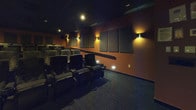 This private theater is thoughtfully designed to deliver an immersive cinematic experience within a compact, single-level screening room. The space is anchored by a large projection screen positioned at the front wall, providing a commanding focal point for all viewers. Rows of plush, reclining leather-style seats are arranged in a tiered, stadium-style layout, ensuring unobstructed sightlines from every position. Each seat features integrated armrests with built-in cup holders, prioritizing comfort during extended screenings.

The interior design emphasizes acoustic performance and visual atmosphere. Large rectangular acoustic panels are mounted strategically across the warm terracotta-toned walls, minimizing sound reflection and enhancing audio clarity. Surround sound speakers are mounted at multiple points along the walls, supporting a full audio environment. The dark ceiling, combined with low-profile recessed lighting and wall-mounted sconces, creates a moody, cinema-appropriate ambiance while providing sufficient illumination in the seating area. Step lighting along the row aisles ensures safe navigation in dim conditions. The dark, textured carpeted flooring ties the room together, completing the dedicated, professional-grade theater aesthetic.