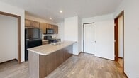 This efficiently designed 2-bedroom, 1-bathroom single-floor unit offers a well-organized layout that maximizes every square foot. The open-concept kitchen anchors the living space with warm, medium-toned wood cabinetry, a peninsula island featuring a double stainless steel sink and laminate countertops, and black appliances including a refrigerator, range, and over-the-range microwave. Light wood-look flooring runs throughout the kitchen and main living areas, creating a cohesive aesthetic. The living room benefits from a ceiling fan and flows directly to a private balcony through sliding glass doors, offering pleasant outdoor views of the surrounding landscape. Both bedrooms feature plush carpeting and large windows that bring in natural light; the primary bedroom provides a comfortable and functional retreat. The full bathroom includes a clean, white soaking tub and shower surround. A dedicated laundry area with a full-size top-load washer and dryer adds everyday convenience. Textured ceilings and warm wood-toned door and window trim are consistent throughout, giving the unit a unified and tidy finish. This unit is a practical and well-appointed space suited for a range of living needs.