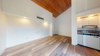 Located at 2106 Corner Lake Dr in Haines City, Florida, this single-story home showcases a distinctive architectural design centered around dramatically vaulted ceilings finished with rich, warm-toned wood planking. This striking overhead detail adds character and visual depth throughout the main living areas, creating an open and airy atmosphere that feels generously spacious.

Light wood-look flooring extends consistently throughout the home, lending a clean, cohesive aesthetic that complements the bright white walls. The main living area is a standout space, featuring the soaring vaulted ceiling, recessed lighting built into a niche along one wall, and a central HVAC vent that ensures year-round comfort. Large sliding glass doors span nearly an entire wall, fitted with vertical blinds to control light and privacy, while offering outdoor views and flooding the interior with natural light.

The hallway connects the various areas of the home with a straightforward, functional layout. Louvered wooden doors add a touch of warmth and traditional charm, contrasting nicely with the otherwise contemporary, minimalist interior. Additional rooms feature the same clean white walls and wood-look flooring, maintaining a consistent and unified design throughout. The kitchen is partially visible, offering a glimpse of white cabinetry and essential appliances. Overall, the home presents a bright, well-maintained, and inviting interior.