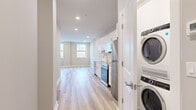 This single-floor unit showcases a clean, modern aesthetic achieved through a thoughtful renovation. Light-toned hardwood flooring runs consistently throughout the space, creating a cohesive and airy feel that connects each room seamlessly.

The kitchen is a standout feature, equipped with white shaker-style cabinetry, light stone countertops, and a classic white subway tile backsplash. A full suite of stainless steel appliances includes a refrigerator, electric range, over-the-range microwave, and dishwasher. A dedicated laundry closet just off the kitchen houses a stacked full-size washer and dryer, adding significant everyday convenience.

The open living and dining area benefits from recessed lighting and natural light supplied by gridded windows, which also offer views of the surrounding neighborhood. Multiple well-proportioned bedrooms feature neutral walls, recessed lighting, and continued hardwood flooring, providing versatile and bright spaces.

The bathroom is finished with large-format marble-look tile flooring, a tub and shower combination with matching tile surround, a white vanity with an integrated sink, and a framed mirror. Throughout the unit, crisp white trim, neutral gray walls, and recessed lighting contribute to a polished, move-in-ready atmosphere.