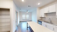 This single-floor unit showcases a clean, contemporary design throughout. The kitchen is a standout feature, equipped with stainless steel appliances including a refrigerator, electric range, built-in microwave, and dishwasher. White shaker-style cabinetry extends to the ceiling, complemented by granite countertops, a subway tile backsplash, and an undermount sink. A large kitchen island with a light-colored surface provides additional workspace and casual dining potential.

The open-concept layout connects the kitchen seamlessly to the living area, which features wood-look flooring, recessed lighting, a ceiling fan, and a window that allows natural light to fill the space. The bedroom offers plush carpeting, a ceiling fan with light fixture, and multiple windows fitted with horizontal blinds. A spacious walk-in closet with wire shelving provides generous storage capacity.

The bathroom is well-appointed with a granite-topped white vanity, an undermount sink, modern fixtures, and wood-look flooring that ties in with the rest of the unit. Throughout the space, a neutral color palette of whites and warm tones creates a bright, cohesive ambiance suited to a variety of interior styles.