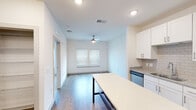 This single-floor unit showcases a clean, contemporary design throughout. The kitchen is a standout feature, equipped with stainless steel appliances including a refrigerator, electric range, built-in microwave, and dishwasher. White shaker-style cabinetry extends to the ceiling, complemented by granite countertops, a subway tile backsplash, and an undermount sink. A large kitchen island with a light-colored surface provides additional workspace and casual dining potential.

The open-concept layout connects the kitchen seamlessly to the living area, which features wood-look flooring, recessed lighting, a ceiling fan, and a window that allows natural light to fill the space. The bedroom offers plush carpeting, a ceiling fan with light fixture, and multiple windows fitted with horizontal blinds. A spacious walk-in closet with wire shelving provides generous storage capacity.

The bathroom is well-appointed with a granite-topped white vanity, an undermount sink, modern fixtures, and wood-look flooring that ties in with the rest of the unit. Throughout the space, a neutral color palette of whites and warm tones creates a bright, cohesive ambiance suited to a variety of interior styles.
