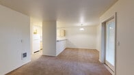 This single-floor residence is designed with a practical, open layout that connects the main living spaces efficiently. The living and dining area is generously proportioned, featuring neutral-toned carpet flooring, textured ceilings, and cream-painted walls that create a clean, understated aesthetic throughout. A pendant light fixture marks the dining zone, while a wall-mounted thermostat and multiple electrical outlets add functional detail.

The kitchen is positioned behind a peninsula-style breakfast bar, offering a natural division between the cooking and living areas. Light wood cabinetry provides ample storage, complemented by a white refrigerator, an electric range, and continuous countertops under flush-mounted fluorescent lighting.

The bedrooms are carpeted and well-sized, each featuring neutral walls and natural light from windows that overlook the exterior. Closet space is accessible directly from the bedroom corridor, with built-in hanging rods providing organized storage.

The bathroom includes a full-size soaking tub with a shower surround, a single-sink vanity with light wood cabinetry, and warm earth-toned tile flooring. The hallway connecting the bedrooms and bathroom is compact and functional, maintaining a cohesive flow throughout the unit.