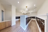 Located at 12121 Greenspoint Drive in Houston, TX, this single-floor mail room is a thoughtfully designed communal facility that combines practicality with modern aesthetics. The space is organized around a central island structure and perimeter-mounted mailbox banks, all finished in a sleek dark bronze tone and set within crisp white framing — creating a clean, high-contrast visual appeal throughout.

The layout maximizes functionality, with rows of individually numbered mailboxes lining both the central island and the surrounding walls, providing ample mail storage capacity for a large residential or mixed-use community. The flooring consists of warm wood-look planks that lend a welcoming, contemporary feel to what is traditionally a utilitarian space.

Overhead, a series of modern sculptural pendant light fixtures with gold brass canopies serve as elegant focal points, complementing the recessed ceiling lighting that ensures the room is well-illuminated. The neutral warm-beige walls and white trim contribute to a bright, airy atmosphere. A glazed entry door allows natural light to filter in from outside, further enhancing the open feel of the space. Clean architectural columns add structural definition without disrupting the room's flow, resulting in a mail room that is as visually refined as it is efficiently organized.