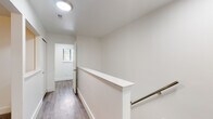 This single-floor space is designed with a clean, modern aesthetic, emphasizing bright, neutral tones and functional layouts throughout. The living area is a generous, open space finished with smooth hardwood-style flooring and anchored by a large sliding glass door that opens to a balcony, allowing abundant natural light and outdoor views to enhance the room's airy feel. Adjacent to the living area, the dining space features warm wood-tone flooring and a modern chandelier, creating an inviting atmosphere. An arched passthrough connects seamlessly to the galley-style kitchen, which is outfitted with light grey cabinetry, white quartz-style countertops, a white subway tile backsplash, stainless steel appliances, and hardwood-style flooring.

The bedrooms are carpeted in neutral tones and well-lit by windows fitted with blinds that frame outdoor greenery. At least one bedroom includes access to a walk-in closet. A hallway with hardwood-style flooring and a staircase railing featuring sleek metal accents connects the living spaces. The bathroom presents a clean, white vanity with a large mirror and standard fixtures. Throughout, crisp white walls, consistent trim work, and carefully chosen finishes contribute to a cohesive and move-in-ready environment.