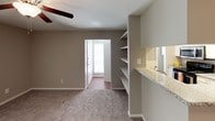 This single-floor residential unit offers a practical and comfortable layout with a cohesive neutral color palette throughout. The galley-style kitchen is well-equipped, featuring white shaker cabinetry, granite countertops, a stainless steel sink, and stainless steel appliances including a refrigerator. Wood-look flooring runs through the kitchen, adding warmth and durability to the space.

The living area is carpeted and open, benefiting from a ceiling fan overhead and a large sliding glass door dressed with vertical blinds that allows natural light to fill the room. Built-in shelving near the kitchen pass-through provides convenient storage and display space.

The bedrooms are carpeted and neutral in tone, each equipped with ceiling fans and windows fitted with blinds for light control. The rooms offer a clean, versatile canvas suitable for a variety of furniture arrangements.

The bathrooms are finished with granite countertops, white cabinetry, and undermount sinks. One bathroom features a well-lit vanity area with mirrors and an adjacent shower stall, while the other includes a bathtub-shower combination with overhead storage cabinets. Throughout, the unit maintains a consistent, functional aesthetic suited for everyday living.