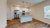 Located in Port Royal, South Carolina, this single-floor residence offers a thoughtfully designed open-concept layout that seamlessly connects the living and kitchen areas. Rich wood-look flooring flows throughout the main living spaces, complemented by warm neutral wall tones and ceiling fans that contribute to a comfortable, airy ambiance. Natural light filters in through multiple windows, enhancing the welcoming atmosphere.

The kitchen is a standout feature, showcasing crisp white shaker-style cabinetry, granite countertops, and a classic white subway tile backsplash. A central island with a sink provides additional workspace and is illuminated by elegant pendant lighting. Stainless steel appliances, including a refrigerator with ice maker, range, and over-the-range microwave, complete this functional and stylish kitchen.

The bedroom features plush carpeting, natural light from dual windows with blinds, and a ceiling fan for year-round comfort. The bathroom is well-appointed with a tub-shower combination, built-in shelving, brushed nickel fixtures, wood-look flooring, white cabinetry, and granite countertops — maintaining a consistent and polished aesthetic. The overall design reflects modern, low-maintenance living in a clean and move-in ready setting.