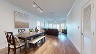 This single-floor residence is designed with an open-concept layout that seamlessly connects the living, dining, and kitchen areas, creating a cohesive and functional living environment. Rich hardwood-style flooring flows throughout the main living spaces, complemented by crown molding and neutral-toned walls that lend a clean, contemporary aesthetic.

The expansive living and dining area is bright and welcoming, featuring track lighting over the dining space and a ceiling fan in the living room. French doors at the far end of the living area invite natural light and provide outdoor access. The dining area comfortably accommodates a large farmhouse-style table with bench seating.

The kitchen is well-equipped with rich dark cabinetry, granite countertops, stainless steel appliances, a center island with pendant lighting, and a tiled backsplash. A stacked washer and dryer unit is conveniently integrated nearby.

The bedrooms are finished with plush carpeting and feature ceiling fans, natural light from windows, and generous closet space, including walk-in closets with wire shelving systems. The bathroom offers dark wood cabinetry, granite counters, a large mirror, and a tiled tub-shower combination.