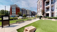 This residential unit is part of a dynamic multi-story community that blends modern living with inviting outdoor amenities. The outdoor cornhole area is a standout communal feature, showcasing a well-maintained artificial turf lawn lined with sleek benches and draped with overhead string lights that create a warm, social atmosphere. The surrounding streetscape includes mature landscaping, classic brick-accented architecture, and open sky views that lend the area a lively yet comfortable feel.

Inside, the unit features a clean, neutral color palette with warm beige tones throughout. Plush carpeting covers the bedroom areas, providing comfort underfoot, while rich hardwood-style flooring flows through the kitchen and bathroom spaces. The kitchen is visible from the living area and features dark cabinetry, granite-look countertops, and pendant lighting that adds a touch of sophistication.

Each bedroom is well-sized, filled with natural light through large windows that offer views of the surrounding greenery. The bathrooms are thoughtfully finished with dark wood vanities, granite countertops, wide mirrors, and a tub-shower combination. Clean white trim and doors throughout the unit provide a crisp, polished contrast to the warm wall tones, creating an overall ambiance that is both functional and welcoming.