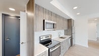 This contemporary single-floor residence is thoughtfully designed with clean lines, modern finishes, and an open, airy layout throughout. The kitchen serves as a functional centerpiece, outfitted with wood-grain cabinetry extending floor to ceiling, crisp white quartz countertops, a white tile backsplash, and a full suite of stainless steel appliances including an electric range, over-the-range microwave, refrigerator, and dishwasher. Light wood-tone flooring flows seamlessly through the living and bedroom areas, complementing the bright white walls that amplify the sense of openness.

The living area is generously proportioned, featuring track lighting and direct sightlines to the kitchen, creating a cohesive and connected layout. The bedrooms are well-sized, each benefiting from tall, large-format windows that frame scenic neighborhood views and invite abundant natural light. The bathrooms are finished in a clean, minimalist style with neutral tile flooring, modern fixtures, and grab bars indicating accessibility-conscious design. A dedicated in-unit laundry closet houses a stacked washer and dryer, adding practical convenience. Overall, this residence presents a polished, move-in-ready interior with a consistent modern aesthetic throughout.