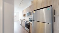 Located at 808 Chapel Street in the heart of New Haven, CT, this efficiently designed single-floor unit offers a thoughtfully arranged layout comprising a living room, kitchen, and bathroom. The interior is finished in a clean, contemporary style with light wood-tone flooring running throughout, crisp white walls, and abundant natural light streaming in through large windows that frame views of the surrounding New Haven streetscape.

The galley-style kitchen is a standout feature, outfitted with light wood laminate cabinetry extending to the ceiling for maximized storage, stainless steel appliances including a full-size refrigerator, electric range, over-the-range microwave, and dishwasher, all set against white countertops. Track lighting overhead adds both functionality and a modern aesthetic touch.

The living area is bright and open, with smooth white walls, recessed lighting, and a sleek sliding glass-panel closet door that contributes to the space's streamlined feel. Large windows invite natural light and provide views of the urban neighborhood.

The bathroom continues the modern design language with wood-toned cabinetry, a white countertop vanity with an integrated sink, a large mirror, wood-look flooring, and clean white walls, creating a bright and functional space. Overall, the unit presents a cohesive, move-in-ready aesthetic well-suited to urban living in New Haven.