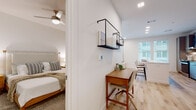This single-floor residence offers a thoughtfully designed open-concept layout with clean, contemporary finishes throughout. The kitchen serves as a central highlight, featuring sleek gray shaker-style cabinetry extending to the ceiling, stainless steel appliances including a range, dishwasher, and French door refrigerator, and a marble-style tile backsplash. A white waterfall-edge island provides additional seating and workspace, while light hardwood flooring and natural light from multiple windows create a bright, airy atmosphere.

The living area is comfortable and well-proportioned, with recessed lighting, light hardwood floors, and large windows dressed with sheer curtains that invite natural light. An adjacent workspace nook features a warm-toned wooden desk and wall-mounted open shelving, offering a functional area for working from home.

The bedroom is carpeted and serene, with neutral walls and a ceiling fan. A walk-in closet with built-in shelving and hanging rods provides ample storage. The bathroom is clean and minimal, finished with light wood-look flooring, a wall-mounted toilet, and simple, modern fixtures. Throughout the unit, a consistent palette of whites, warm woods, and soft grays creates a cohesive and inviting ambiance.
