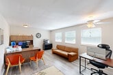 Located at 1151 Roger Ave in Swansea, Illinois, this single-floor space offers a well-organized and efficiently utilized layout that combines a kitchen and living area into one cohesive unit. The interior is finished with light wood-tone luxury vinyl flooring throughout, contributing to a clean and modern aesthetic against crisp white walls.

The main area serves a dual purpose as both a functional office and a comfortable reception space. It features a built-in wood-toned desk unit with overhead cabinetry, a computer workstation, and a black multi-function printer housed on a matching filing cabinet. A tan leather sofa and additional seating provide a welcoming area for visitors, while a ceiling fan with light fixture and multiple flush-mount lights ensure the space is well illuminated. A row of three windows along one wall floods the room with natural light, with white horizontal blinds offering adjustable privacy.

The kitchen area is neatly appointed with white shaker-style cabinetry, light granite-look countertops, a stainless undermount sink, and black appliances including a refrigerator, range, and over-the-range microwave. A window above the sink brings in additional natural light. The overall ambiance of the space is bright, tidy, and professional, making it well-suited for a small business or office setting.