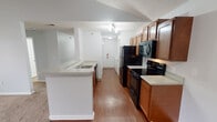 This single-floor residence offers a functional and comfortable layout designed for everyday living. The galley-style kitchen is outfitted with warm medium-toned wood cabinetry, light countertops, and a full suite of black appliances including a refrigerator, electric range, built-in microwave, and dishwasher. A peninsula with a double sink separates the kitchen from the rest of the living space, creating an open, connected flow throughout. The living area is generously sized, featuring plush carpeting, vaulted ceilings, and a ceiling fan. A tile-surround fireplace anchors one end of the room, while a sliding glass door fills the space with natural light and provides access to an outdoor view. A hallway connects the main living areas to the bedrooms and bathrooms. The primary bathroom includes a walk-in shower with a built-in bench, while a second full bathroom offers a tub-shower combination and stone-look tile flooring. A spacious walk-in closet with wire shelving provides ample storage. The unit also includes an in-unit laundry area and a utility hallway with wood-look flooring that extends throughout the kitchen and entry corridor. Overall, the space offers a clean, practical design with consistent finishes throughout.