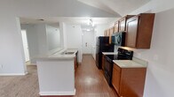 This single-floor residence offers a functional and comfortable layout designed for everyday living. The galley-style kitchen is outfitted with warm medium-toned wood cabinetry, light countertops, and a full suite of black appliances including a refrigerator, electric range, built-in microwave, and dishwasher. A peninsula with a double sink separates the kitchen from the rest of the living space, creating an open, connected flow throughout. The living area is generously sized, featuring plush carpeting, vaulted ceilings, and a ceiling fan. A tile-surround fireplace anchors one end of the room, while a sliding glass door fills the space with natural light and provides access to an outdoor view. A hallway connects the main living areas to the bedrooms and bathrooms. The primary bathroom includes a walk-in shower with a built-in bench, while a second full bathroom offers a tub-shower combination and stone-look tile flooring. A spacious walk-in closet with wire shelving provides ample storage. The unit also includes an in-unit laundry area and a utility hallway with wood-look flooring that extends throughout the kitchen and entry corridor. Overall, the space offers a clean, practical design with consistent finishes throughout.