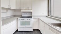 Located on the 12th floor at 3470 Rue Stanley in the heart of downtown Montréal, this unit offers a well-organized layout comprising a living room, kitchen, bathroom, and two hallways. The living room is the standout space, bathed in abundant natural light through expansive floor-to-ceiling windows that wrap around the room, framing impressive panoramic views of the Montréal skyline. A wall-mounted air conditioning unit and access to a balcony further enhance the living area's comfort and functionality. The classic parquet wood flooring throughout the living spaces adds warmth and timeless character to the bright, white-painted interior. The kitchen is efficiently designed with white cabinetry, ample counter space, dark slate-style tile flooring, and white appliances including an electric range, providing a clean and practical cooking environment. The bathroom features neutral mosaic tile flooring and wall tiling, a full soaking tub with overhead shower, and a clean, understated aesthetic. Two hallways connect the spaces, contributing to a logical and functional flow throughout the unit. Overall, the space presents a bright, airy ambiance with urban views and classic architectural details in one of Montréal's most central and vibrant neighborhoods.