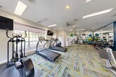 Located at Lenox Park in Brookhaven, Georgia, this well-equipped fitness center offers a comprehensive exercise environment designed to support a full range of workout routines. The single-floor space is thoughtfully organized to maximize functionality, with distinct zones for cardio, strength training, and stretching.

The cardio section is furnished with multiple treadmills, elliptical trainers, and a stationary bike, all positioned near large windows fitted with soft Roman shades that allow natural light to filter in while maintaining privacy. Two wall-mounted flat-screen televisions provide entertainment during workouts.

The strength training area features a cable and pulley multi-station machine, a weight bench, a rack of dumbbells and kettlebells, and an assortment of medicine balls and stability balls displayed along a vibrant accent wall bearing the Lenox Park branding. A large floor-to-ceiling mirror amplifies the sense of space and allows users to monitor their form.

Throughout the space, the eye-catching multicolored carpet—featuring bold blue, yellow, and gray geometric patterns—adds a modern, energetic aesthetic. Recessed lighting and overhead panel lights ensure bright, consistent illumination, while a ceiling fan promotes air circulation. The overall ambiance is clean, organized, and motivating, providing residents with a convenient and well-appointed place to pursue their fitness goals.
