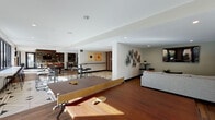 Located at 2200 John Muir Pkwy in Hercules, California, this single-floor community amenity space is designed to serve as a dynamic social and recreational hub. The layout flows seamlessly across several distinct zones, each offering a unique function while maintaining a cohesive contemporary aesthetic.

The game room is a standout feature, equipped with a red-felt pool table, a foosball table, and a ping-pong table, all set atop rich hardwood-style flooring. A bold accent wall in deep red anchors the space, complemented by decorative bicycle wheel art and a wall-mounted flat-screen TV. Adjacent to this area, a comfortable lounge features a large sectional sofa, a flat-screen TV, and vintage sports-themed wall art, creating a relaxed, inviting atmosphere.

The wet bar area is finished with sleek quartz countertops, wood-toned cabinetry, an industrial-style stainless steel sink, textured tile backsplash, and open pipe-and-wood shelving displaying glassware and decanters — ideal for entertaining.

A bright social dining area showcases a striking geometric black-and-white tile floor, round high-top tables with modern stools, and expansive floor-to-ceiling windows that flood the space with natural light and provide views of the exterior courtyard. A wall-mounted TV and direct outdoor access complete this versatile gathering area.
